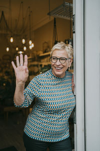 Happy female entrepreneur waving while standing at doorway of store