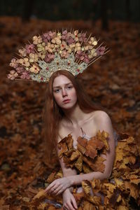 Portrait of young woman wearing flowers on hair sitting at forest during autumn