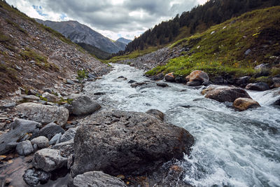 Scenic view of stream flowing through rocks against sky