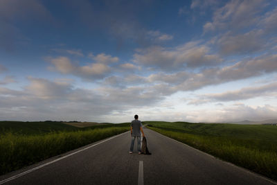 Rear view of man on road amidst field against sky