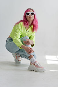 Full length of young woman wearing sunglasses while standing against white background