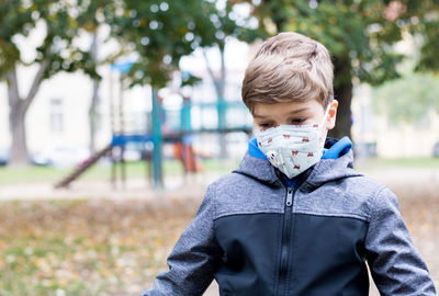 Sad boy wearing face mask while feeling lonely on the playground during coronavirus pandemic.