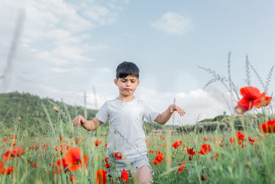 Portrait of young woman picking flowers on field against sky