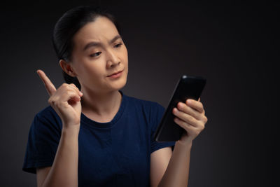 Young woman using smart phone against black background