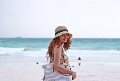 Side view portrait of smiling young woman standing at beach