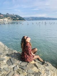 Woman sitting on rock by sea against sky