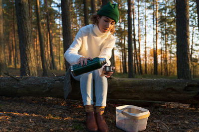 Girl rest from picking mushroom and berries in autumn forest warm up with tea or coffee from thermos