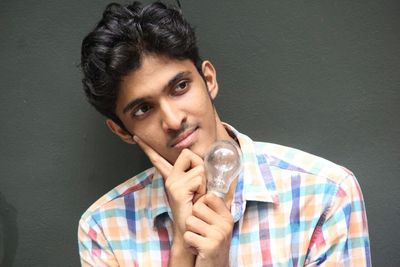 Thoughtful young man with light bulb against gray wall