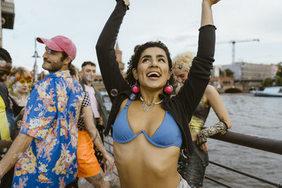 Happy non-binary person dancing with arms raised near friends in city