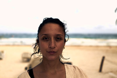 Portrait of young woman standing at beach against sky