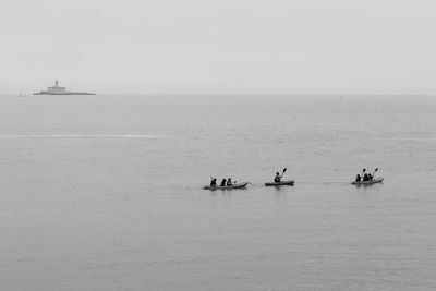 Distant view of people canoeing on sea against sky