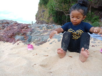 Full length of cute girl sitting on sand at beach