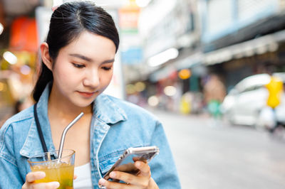 Portrait of young woman using mobile phone in city