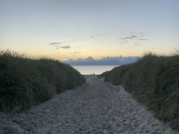 Footpath amidst sea against sky during sunset