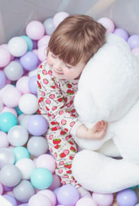 Caucasian beautiful baby girl playing in the playpen with many pastel colored balls and bear toy