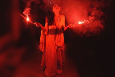 Woman with illuminated sparkler while standing on road at night