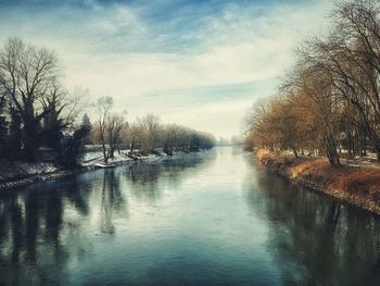 River amidst bare trees against sky during winter