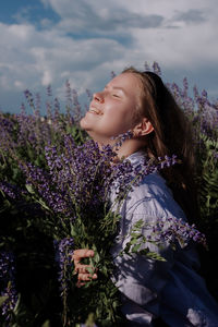 Smiling caucasian young woman with bouquet of purple flowers in field