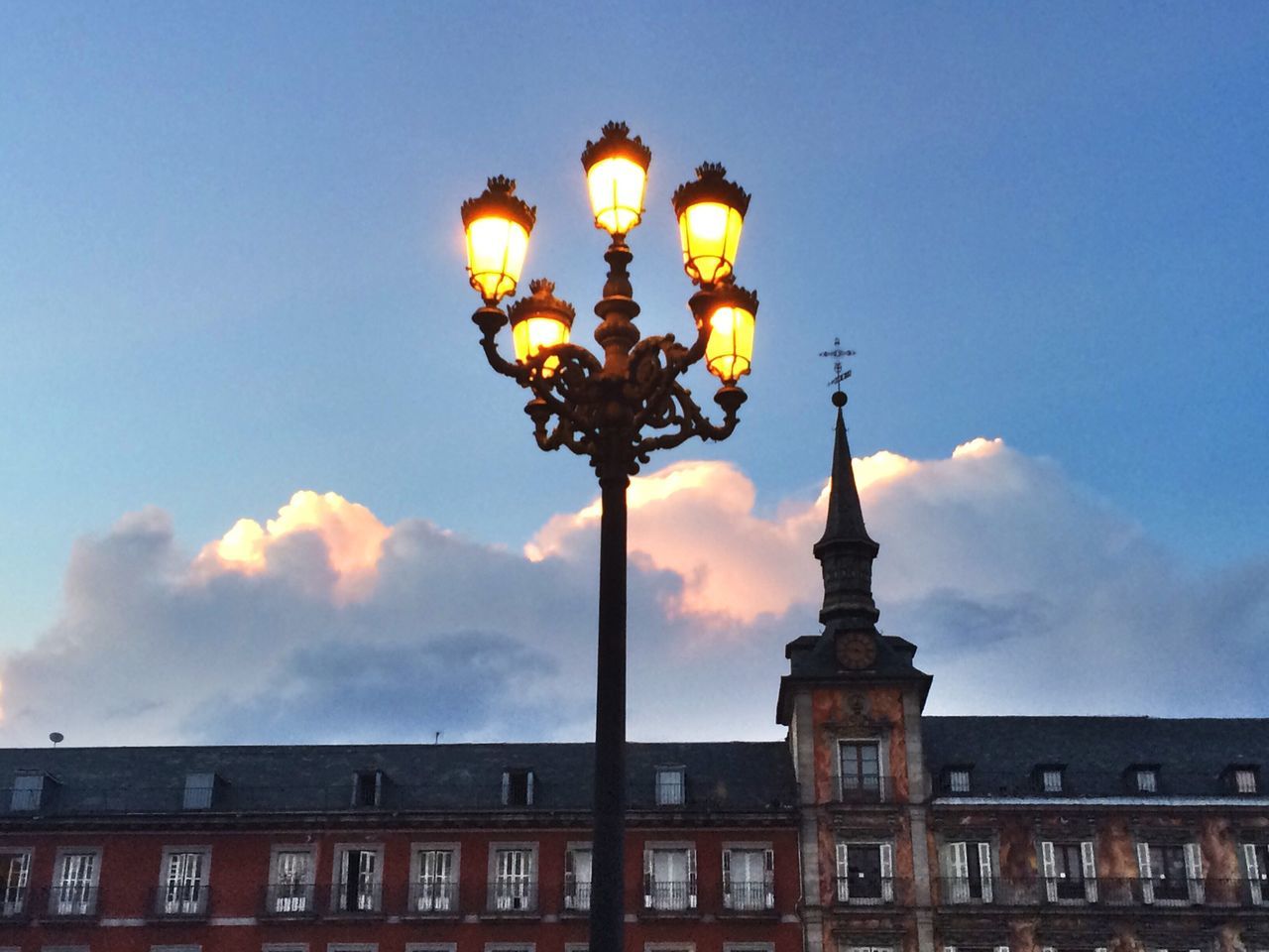 low angle view, architecture, built structure, building exterior, lighting equipment, street light, sky, illuminated, lantern, clear sky, blue, outdoors, dusk, no people, lamp post, building, electric light, city, hanging, high section