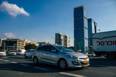 Cars on road by buildings against blue sky