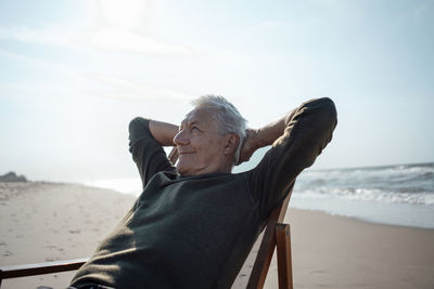 Smiling senior man with hands behind head relaxing at beach