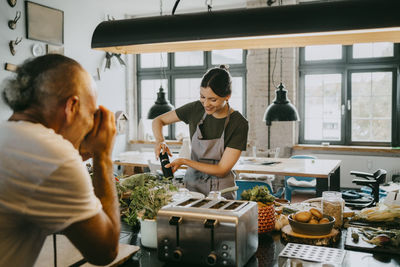 Smiling young female chef preparing food with photographer taking picture in studio kitchen