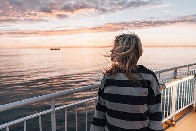 Rear view of woman standing by railing against sea