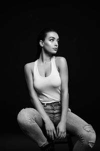 Portrait of woman sitting against black background