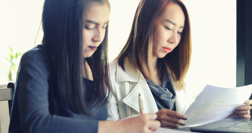 Young women discussing over graphs while sitting on table at office