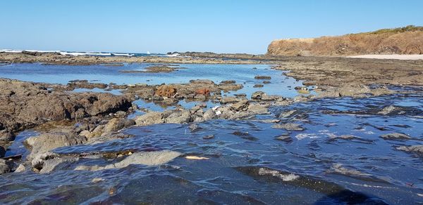 Rock formations in sea against clear blue sky