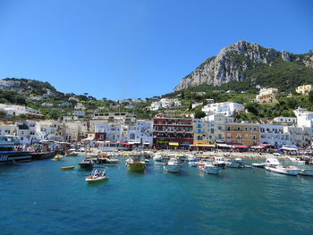 Sailboats in sea by townscape against clear blue sky