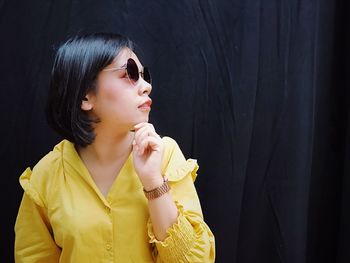 Young woman looking away while standing against black background