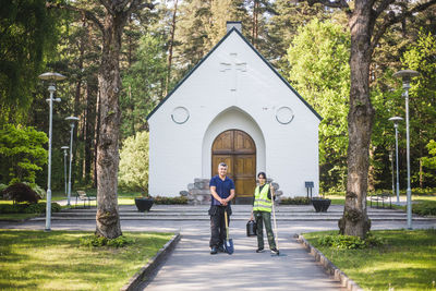 Full length portrait of confident male instructor with young female trainee holding gardening equipment and standing on