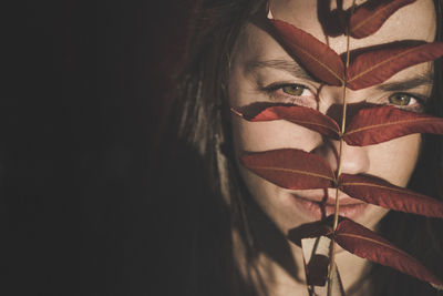 Close-up portrait of young woman covering face with leaves in darkroom