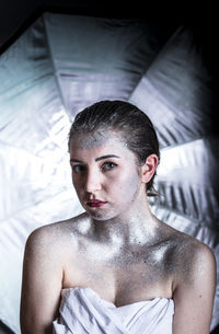 Portrait of young woman covered with glitter against curtain