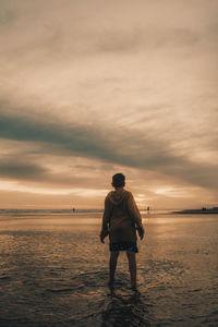 Boy standing contemplating sunset in the beach during sunset