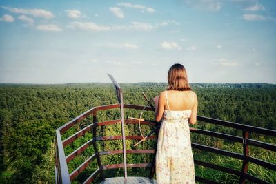 Rear view of woman standing at observation point against forest