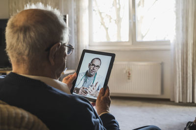 Rear view of man and woman using mobile phone at home