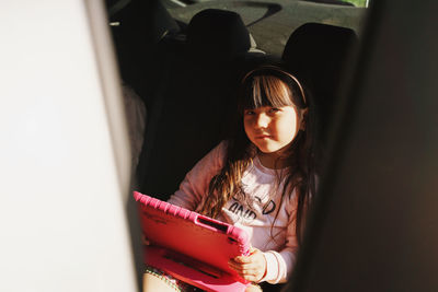 Portrait of girl sitting in car and holding tablet