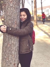 Smiling young woman hugging tree trunk at park