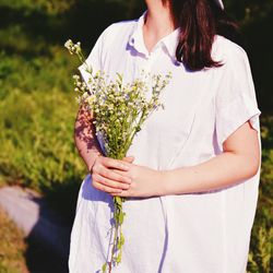 Midsection of woman holding flowers on field