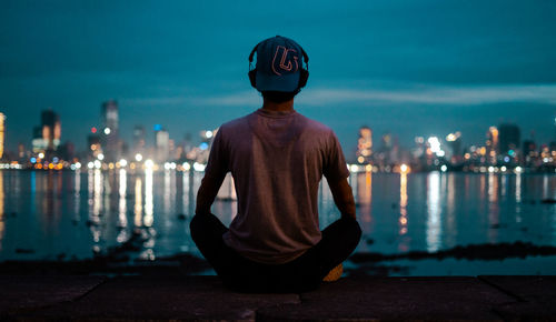 Man sitting in illuminated city against sky at night