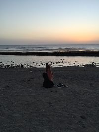 Woman sitting on beach against sky during sunset