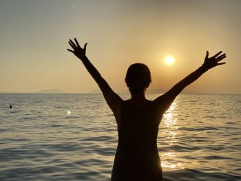 Rear view of silhouette person standing in sea against sky during sunset