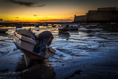 Boats moored on shore against sky during sunset