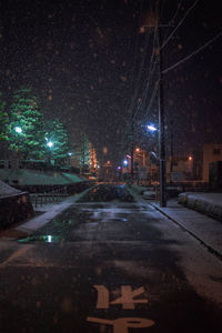 Illuminated street amidst buildings in city during winter at night