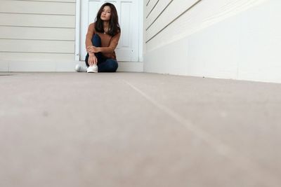 Portrait of young woman sitting by white wall