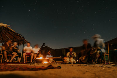 People sitting in illuminated traditional clothing against sky at night