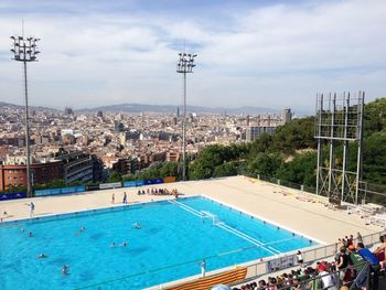 Audience looking at water polo with cityscape against sky