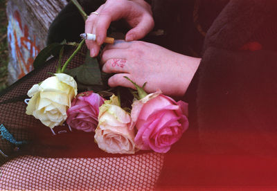 Midsection of woman holding cigarette with rose flowers